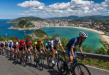 Clássica San Sebastián 2025/2026: O Guia Definitivo para Virar Expert na Clássica Basca Pelotão profissional da Clásica San Sebastián pedalando pela costa do País Basco com a praia de La Concha e a baía de San Sebastián ao fundo em dia ensolarado de verão