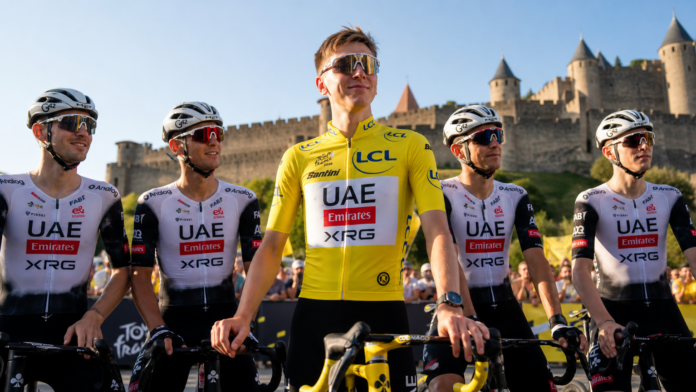 pogacar-amarelo-stage-4-carcassonne-2026 Tadej Pogacar com a camisa amarela de líder ao lado da equipe UAE Emirates-XRG em Carcassonne, fortaleza medieval ao fundo, preparação para a Stage 4 do Tour de France 2026